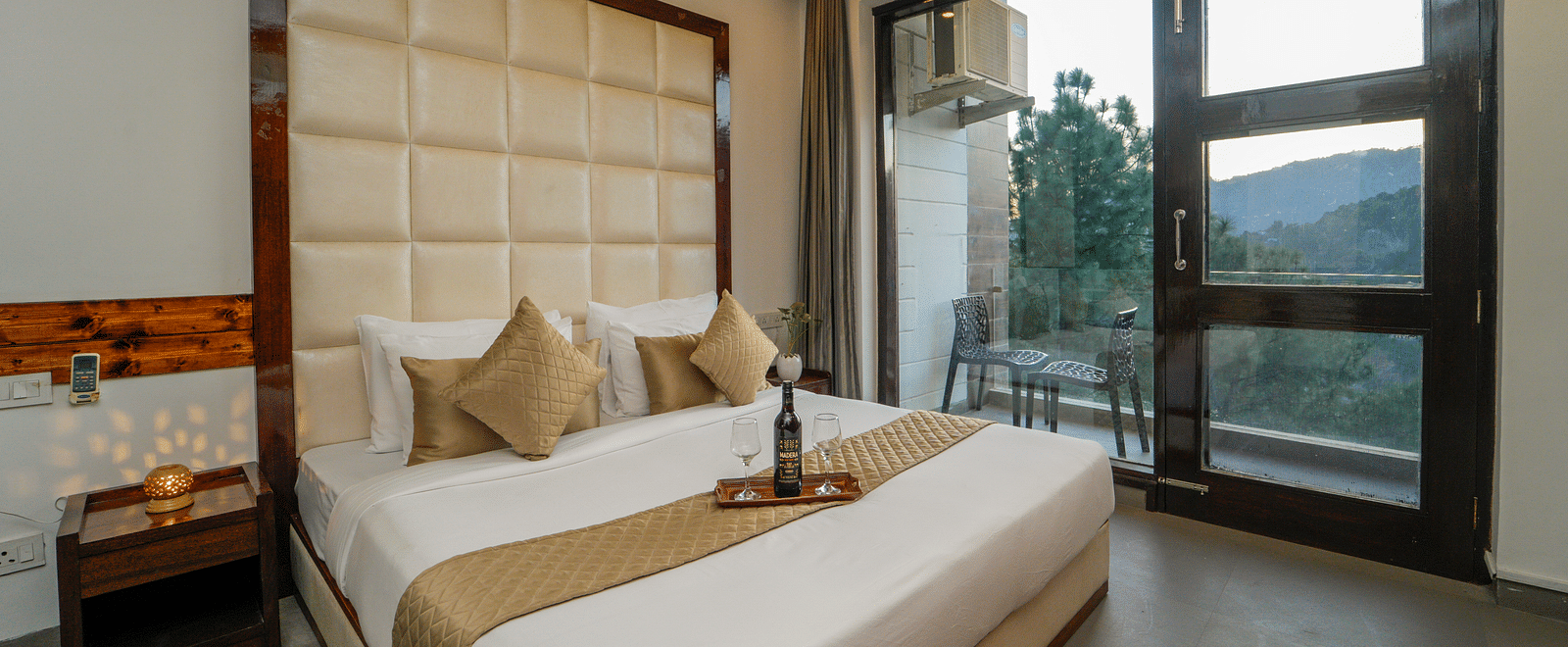 The premium room of DLS Whispering Winds with a bed, bed side tables, and a glass door leading to the balcony overlooking the mountain view